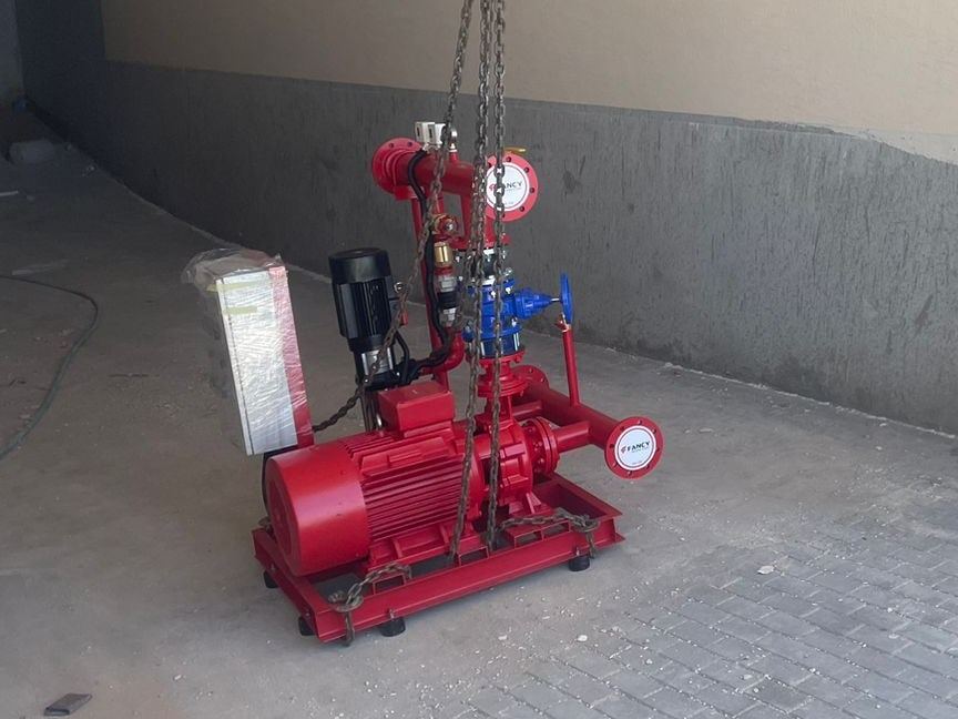 Red fire-pump set with an electric main pump, a jockey pump and controller, suspended from lifting chains