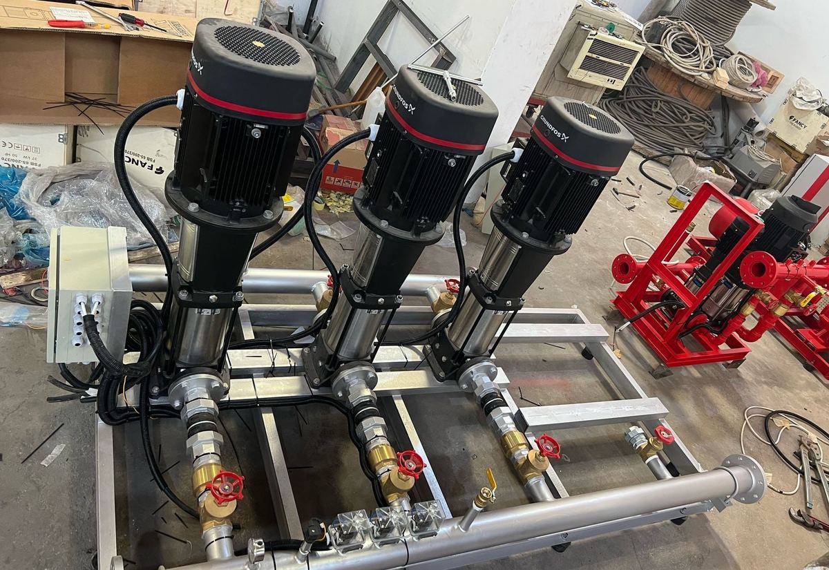 Three Grundfos vertical pumps on a booster skid with its control box, under assembly on the workshop floor