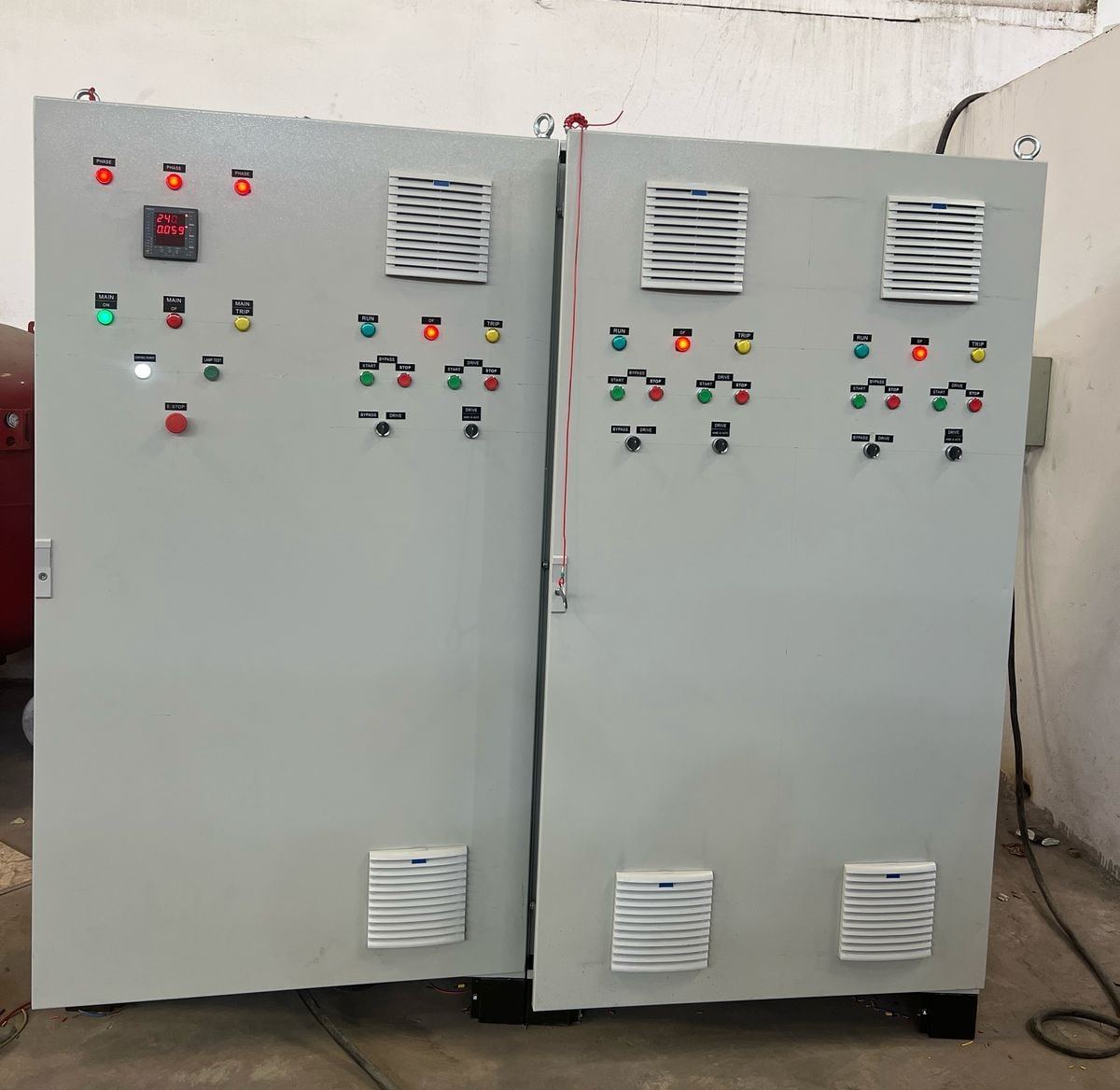 Two finished pump control panels side by side in the workshop, pilot lights lit