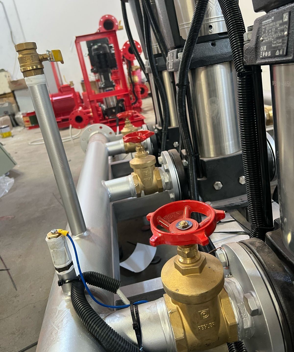 Close-up of gate valves, pipework and pump bases on a booster set in the workshop