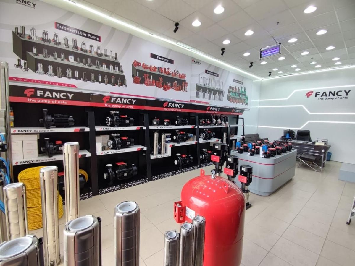 A wall of pump display bays and posters in the Madinah showroom, a red pressure vessel in front