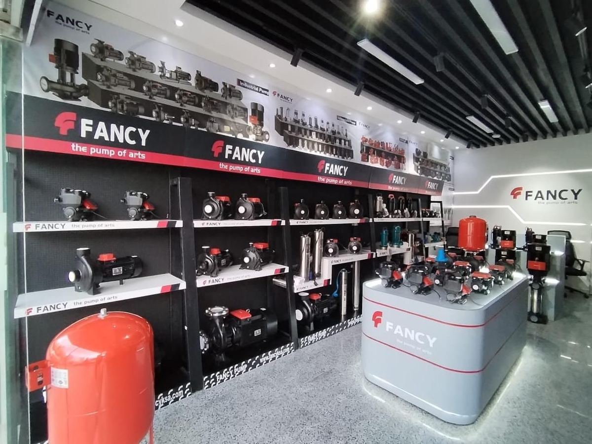 A wall of black display bays holding pumps in the Riyadh showroom, with a red pressure vessel in front