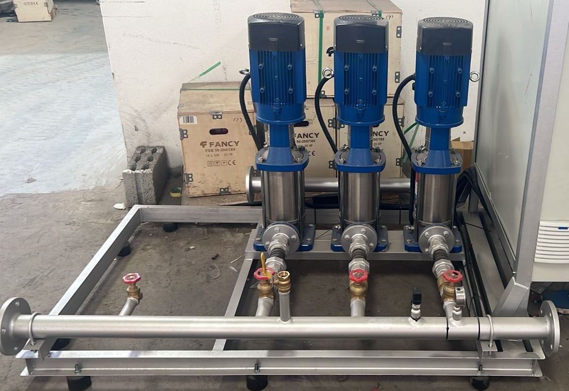 Booster set: three vertical multistage pumps, valves and header on a steel skid beside its control panel