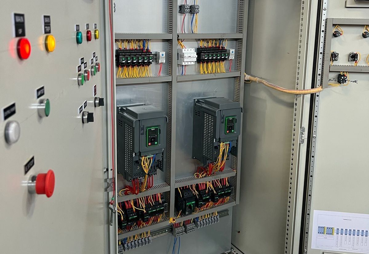 Open pump control panel with two variable-speed drives, relays and terminals; door lamps and emergency stop